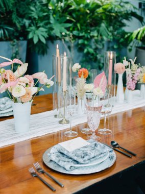 Güzel düzenlenmiş bir yemek masasında canlı çiçekler, zarif cam eşyalar ve yemyeşil mumlar bulunur. Özel bir toplantı veya kutlama için ideal..