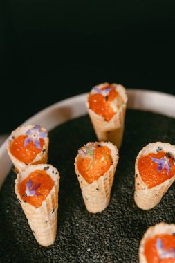 Canlı turuncu yumurta ve yenilebilir çiçeklerle dolu narin deniz ürünleri konileri akşam yemeklerinde zarif bir görüntü oluşturur..