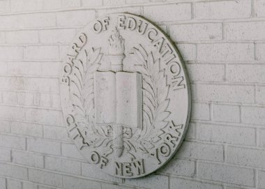 Bir taş amblem, öğrenmeyi ve toplumsal değerleri sembolize eden bir New York eğitim binasının girişini simgeliyor..