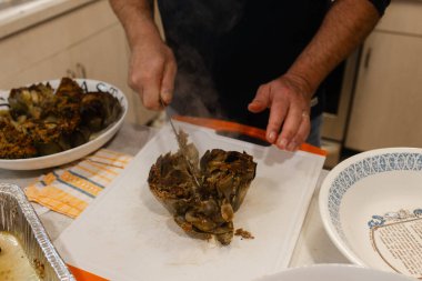 Aile yemeği hazırlıkları sırasında sıcak bir mutfakta içi doldurulmuş enginarı ustalıkla kestiler..