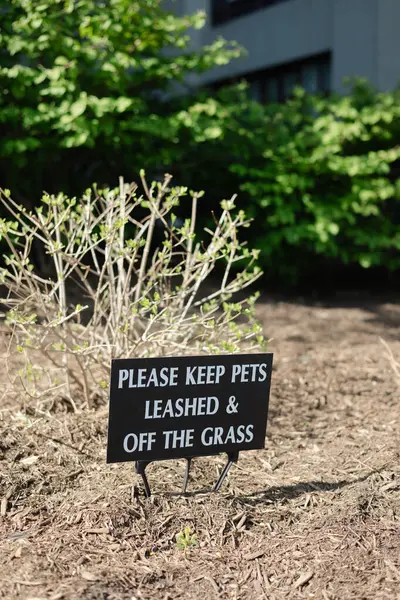 Siyah bir tabela, evcil hayvan sahiplerinden evcil hayvanları iyi korunmuş bir bahçe alanında çimlerin üzerinde ve dışında tutmalarını istiyor..