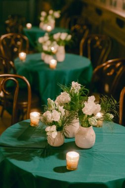 Yeşil ketenle örtülü masalar beyaz çiçekler ve mumlarla süslenerek akşam yemeği için sıcak bir ortam yaratılıyor..