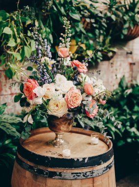 Güllerden ve yeşilliklerden oluşan canlı bir çiçek dizilimi büyüleyici bir iç mekanda ahşap bir fıçı süslüyor..