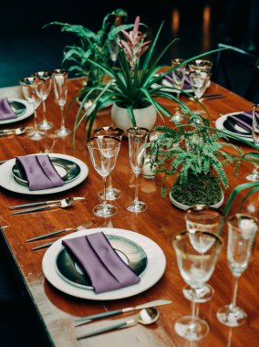 Cam kaplama, siyah tabaklar, mor peçeteler ve dekoratif bitkilerle güzel bir yemek masası misafirleri bekliyor..