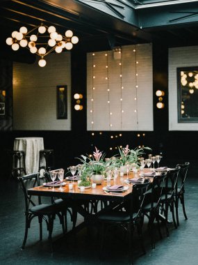 Uzun ahşap bir masa şık bir ortamda çiçekler ve bardaklarla süslenir. Özel bir kutlama gecesi için mükemmeldir..