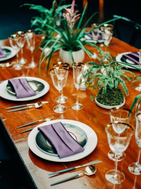 Mor peçeteler, parlak bardaklar ve akşam yemeği için dekoratif bitkilerle çarpıcı bir yemek masası..