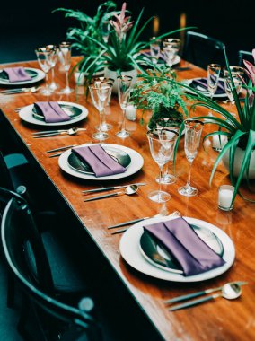 Güzel düzenlenmiş bir yemek masası konukları bekliyor. Sıcak bir atmosferde mor peçeteler ve yemyeşil süsler sergileniyor..