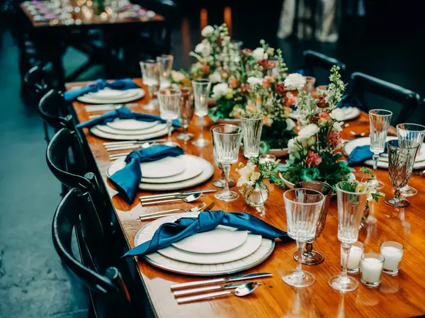 Çiçekler, cam eşyalar ve çatal bıçaklarla süslenmiş zarif yemek masasına bakın. Akşam misafirleri için hazır..