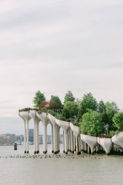 Su üzerinde yükselen şehir parkı yapısı, bulutlu gökyüzü ile sakin bir günde yemyeşil ile çevrili..