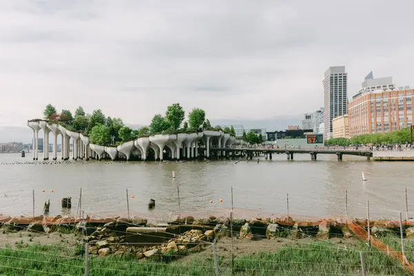 Ziyaretçiler modern mimari ve Hudson Nehri kıyısı boyunca yemyeşil ağaçlarla manzaralı nehir manzarasının tadını çıkarıyorlar..