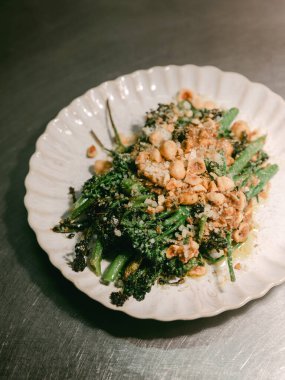 Pişmiş yeşil sebzelerin rengarenk çeşitleri, beyaz bir tabakta çıtır çıtır sunuluyor..