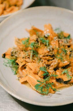 Zengin soslu ve otlarla süslenmiş makarna şık bir restoranda bir tabakta duruyor..