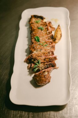 Dilimlenmiş et, taze otlarla süslenmiş beyaz bir tabakta yemek alanında servis edilmeye hazır bekliyor..