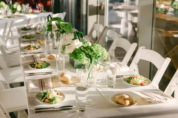 Salatalar, su bardakları ve toplanma için taze sebzelerle dolu uzun bir masa seti..