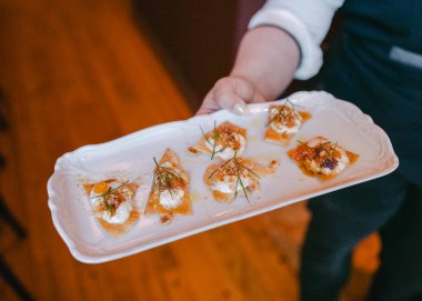 Sunucu, leziz bir şekilde hazırlanmış bir gurme aperatifi sunar. İçinde kremalı soslar ve taze otlar vardır..