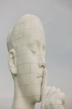 Çarpıcı bir heykel, açık hava ortamında dudaklarında bir parmak ile bir figür tasvir eder..