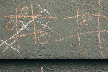Tebeşir tik-tac-toe oyunlarının renkleri ve desenleri gündüz oynarken gri bir duvar süslüyor.