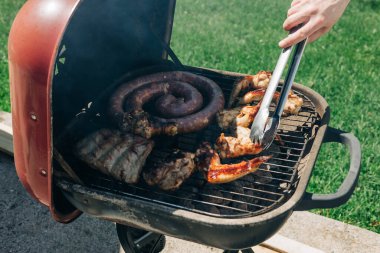 Dostlar bir ızgaranın etrafında toplanır, güneşli bir günde sosis, tavuk ve pirzola gibi çeşitli etleri pişirirler..