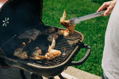 Tavuk kanatları ve kaburgalar güneşli bir günde açık havada ızgara ediliyor, canlı bir barbekü atmosferi sergiliyorlar..