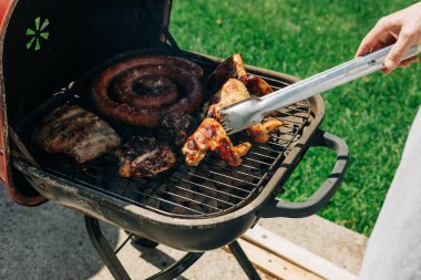 Parlak, güneşli bir havada arka bahçede tavuk kanadı, sosis ve biftek de dahil olmak üzere ızgara et..