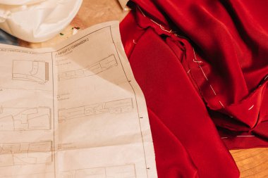 Ayrıntılı bir dikiş şablonu canlı kırmızı kumaşın yanında duruyor. Yaratıcı bir giysi yapımı projesinin hazırlıklarını gösteriyor..