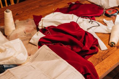 Parlak kırmızı kumaş ve dikiş desenleri ahşap bir masaya saçılmıştır..