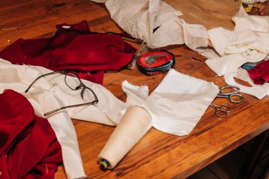 Çeşitli kumaşlar, makas ve dikiş aletleri işlek bir dikiş atölyesinde ahşap bir masaya yayılır..
