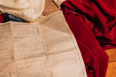 Kırmızı kumaş, ahşap bir masanın üzerinde dikiş desenleri ile serili. Yaratıcı bir zanaat anı sergiliyor..