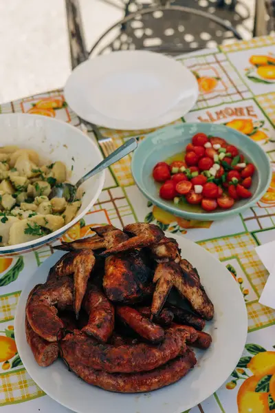 Lezzetli ızgara etler sıcak güneş ışığı altında canlı bir açık hava ortamında taze salata ve makarnaya eşlik eder..