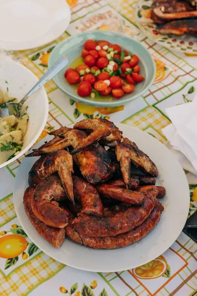 Lezzetli bir tabak ızgara sosis ve tavuk kanadı. Yanında da açık hava etkinliğinde taze domates salatası..