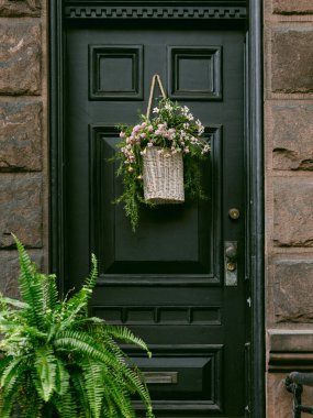 Örülmüş çiçek sepeti ve yeşil eğreltiotu olan şık siyah bir kapı şehirde sıcak bir karşılama sunar..