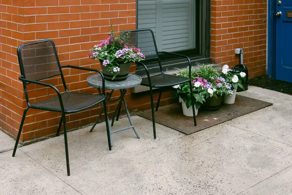 İki sandalye ve bir tuğla binanın mavi kapısının yanında canlı saksılarla çevrili küçük bir masa..