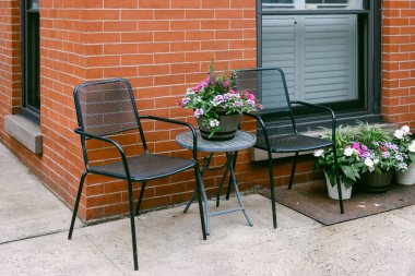 Renkli çiçekler veranda masasını ve yakındaki tencereleri süsler, dışarıda dinlenmek ve eğlenmek için hoş bir yer yaratır..