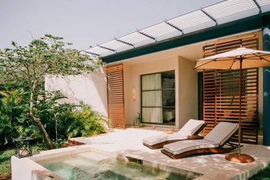 Huzurlu bir öğleden sonrası için yemyeşil yemyeşil bir havuzun yanında zarif şezlongları olan modern villa..