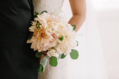 Bir gelin zarif pastel çiçekleri ve yeşillik buketini kapalı bir düğün töreninde sergiliyor..