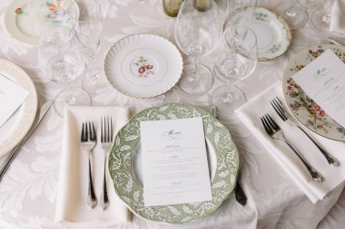 Masa zarif tabaklar, bardaklar ve menülerle resmi bir akşam yemeği için hazırlanmıştır..