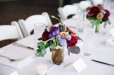 Büyüleyici bir yerdeki düğün kutlaması sırasında canlı çiçek aranjmanları masaları aydınlatır..