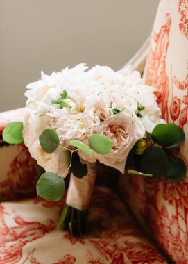 Beyaz çiçekli ve yumuşak yeşillikle hazırlanmış gelin buketi eski bir sandalyede duruyor, düğün zarafetini yakalıyor..