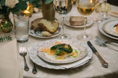Süslü bir yemek masasında şarap ve hafif ışıklandırmayla taze malzemeler içeren kaplanmış gurme tabağı..