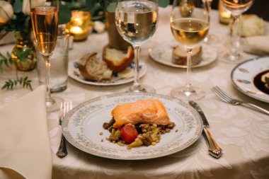 Sebze ve şarapla servis edilen lezzetli somon. Mumlar ve çiçeklerle güzel bir yemek masasında..