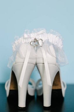 Nazik bir jartiyeri olan beyaz topuklu ayakkabılar. Özel bir düğün gününde gelinlik giymek için mükemmel bir kalp cazibesi..