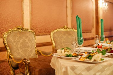 Süslü sandalyeler, lüks bir yemek salonunda pahalı yemekler ve pırıl pırıl camlarla süslenmiş gösterişli bir masa çerçevesi oluştururlar..