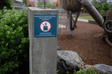 Uyarı levhası, bulutlu bir havada parktaki oyun ekipmanlarına tırmanmanın güvenlik kurallarını vurguluyor.