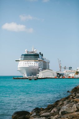 Muhteşem bir yolcu gemisi açık mavi sular ve kayalık bir kıyı şeridiyle çevrili limanda demirlemiş durumda..