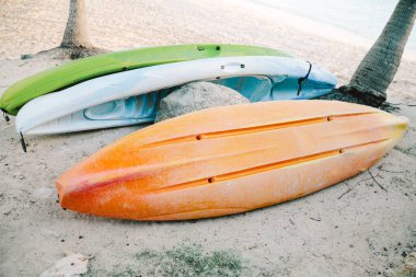 Parlak renkli kanolar palmiye ağaçlarının yanındaki kumda dinleniyor ve sahile gidenleri suyun tadını çıkarmaya davet ediyor..