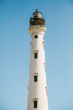 Beyaz bir deniz feneri görkemli bir şekilde mavi gökyüzüne karşı yükseliyor ve gemilere sahil boyunca güvenli bir şekilde rehberlik ediyor..
