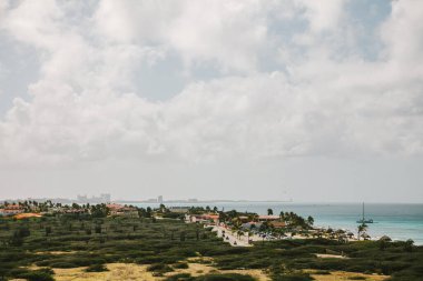 Güzel bir sahil manzarası, canlı yeşillikler ve bulutlu bir gökyüzünün altında sakin suları barındırır..