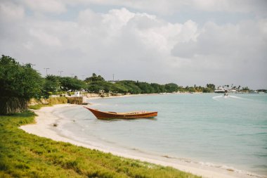 Kırsal ahşap bir tekne kumlu sahilde, bulutlu bir gökyüzünün altında dinlenirken, dalgalar kıyıya vuruyor..