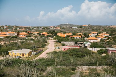 Bereketli yeşil çevre, parlak mavi gökyüzünün altında parlak turuncu çatıları olan sessiz bir mahalleyi vurguluyor..