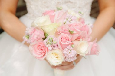 Bir gelin neşeyle pembe ve beyaz güllerle dolu bir buket tutar düğün gününün güzelliklerini yakalar.